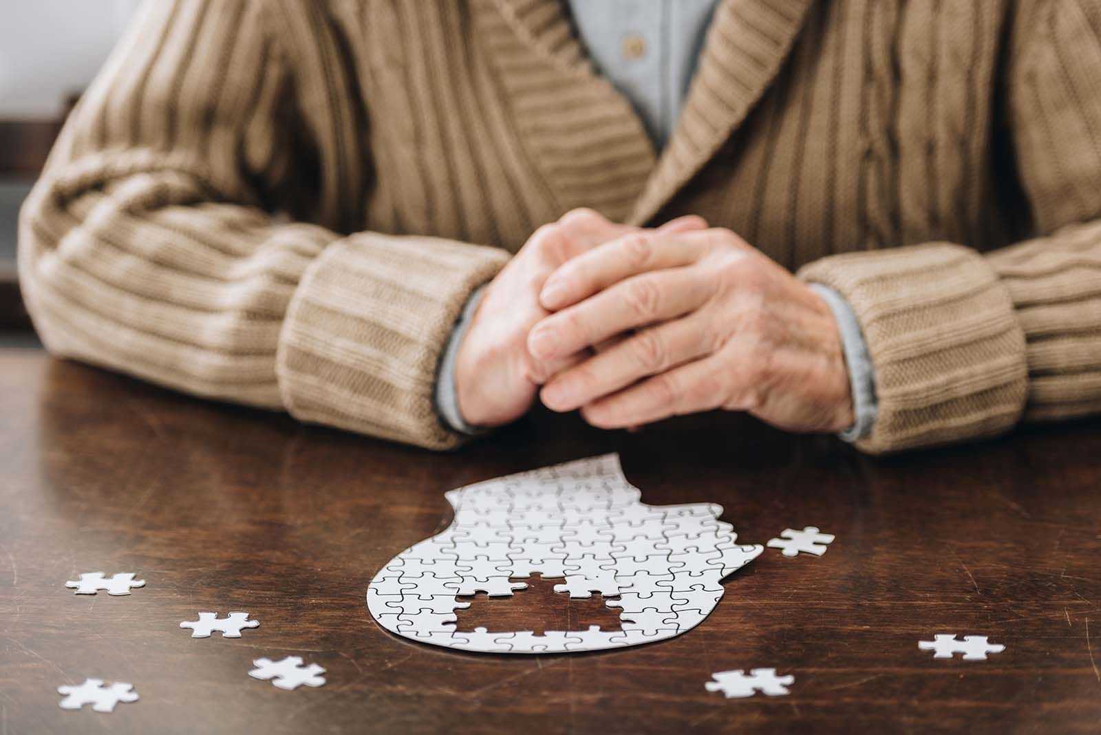 Auf dem Bild ist ein älterer Mann zu sehen, der ein Puzzle hält, das einen Kopf widerspiegelt. Das Gehirn fehlt.