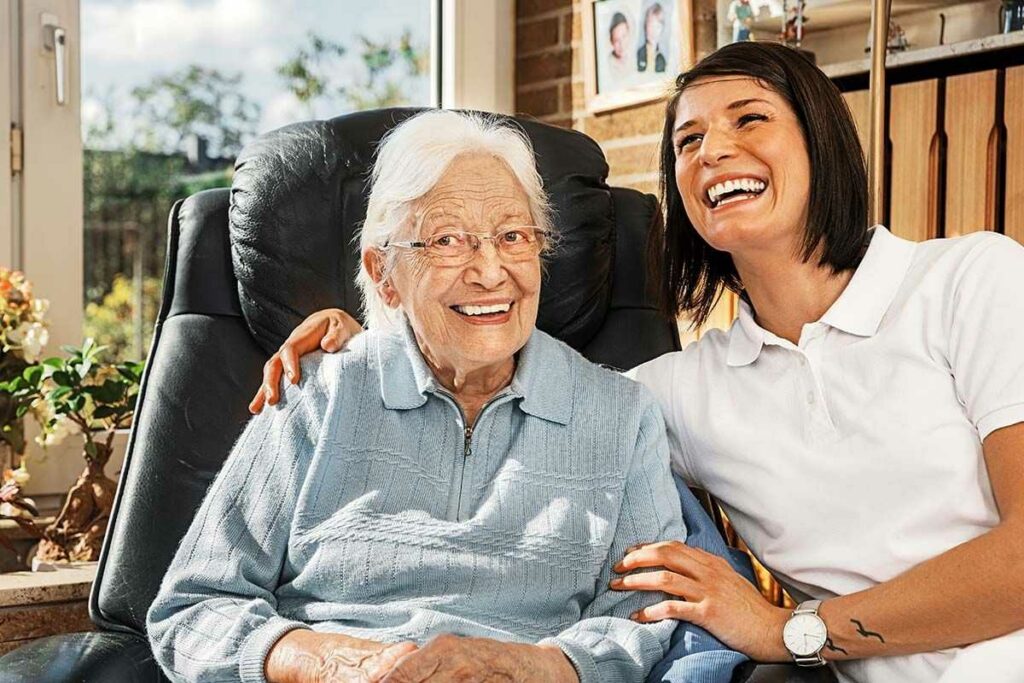 Ältere Frau und ihre Pflegerin lachen zusammen.
