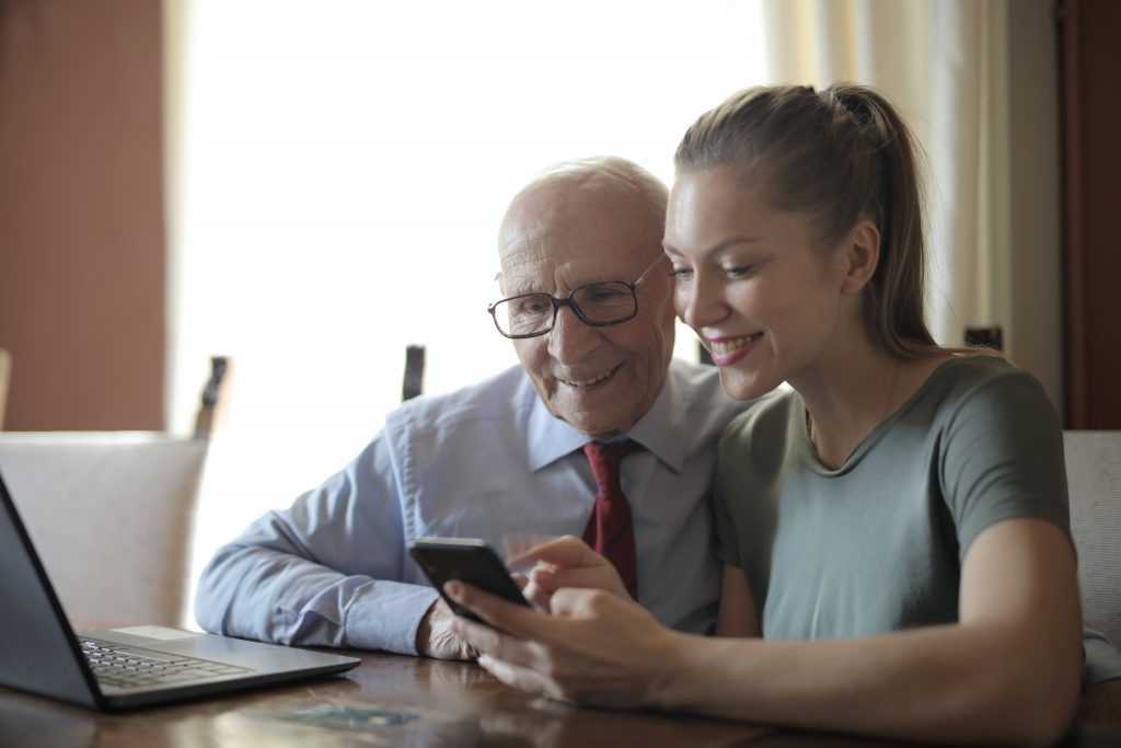Eine junge Frau und ihr Opa schauen sich ein Handy an.